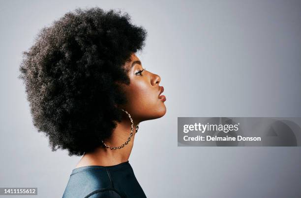 profilo laterale di una bella giovane donna nera che pensa e sembra potente in piedi su uno sfondo grigio dello studio. una splendida e seria femmina afroamericana con un aspetto afro potenziato - profilo vista laterale foto e immagini stock