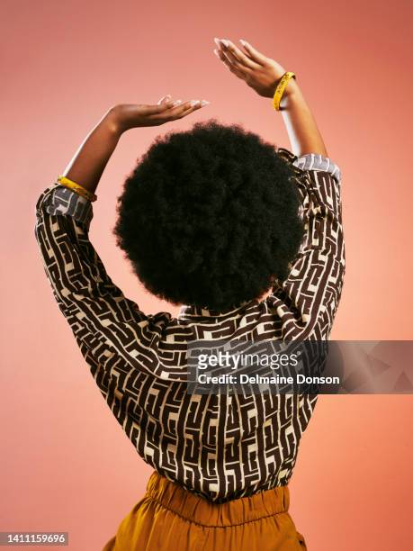 unbeschwerte modische retro-frau, die tanzt, musik hört und spaß hat. porträt von hinten von einer funky und stilvollen frau mit afrohaaren isoliert auf braunem hintergrund. - afro stock-fotos und bilder