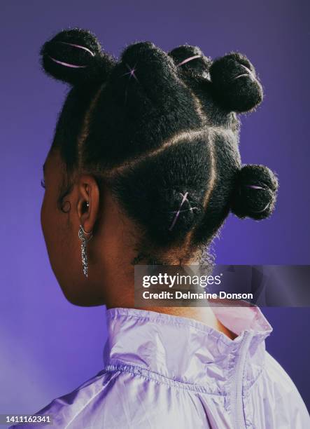 black woman standing against a purple studio background and showing her trendy and funky new hairstyle from behind. one female showing the back of her head with a creative and stylish hairdo - zwart haar stockfoto's en -beelden