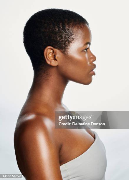 輝く肌を持つ白い背景に孤立した自信に満ちたアフリカ人女性のサイドプロファイル。スキンケアや天然化粧品を促進するために暗い完璧な肌と剃毛された頭を示す深刻な女性 - shaved head ストックフォトと画像