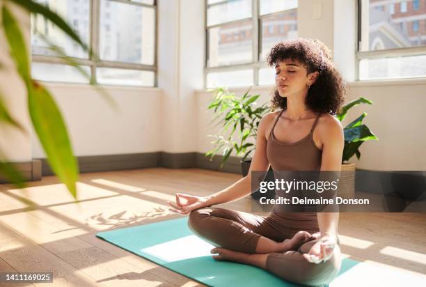 young peaceful woman meditating for relaxation and calmness in the lounge at home. one serious female doing meditation and praying for peace early in the morning. lady relaxing with quiet time - upright position stock pictures, royalty-free photos & images