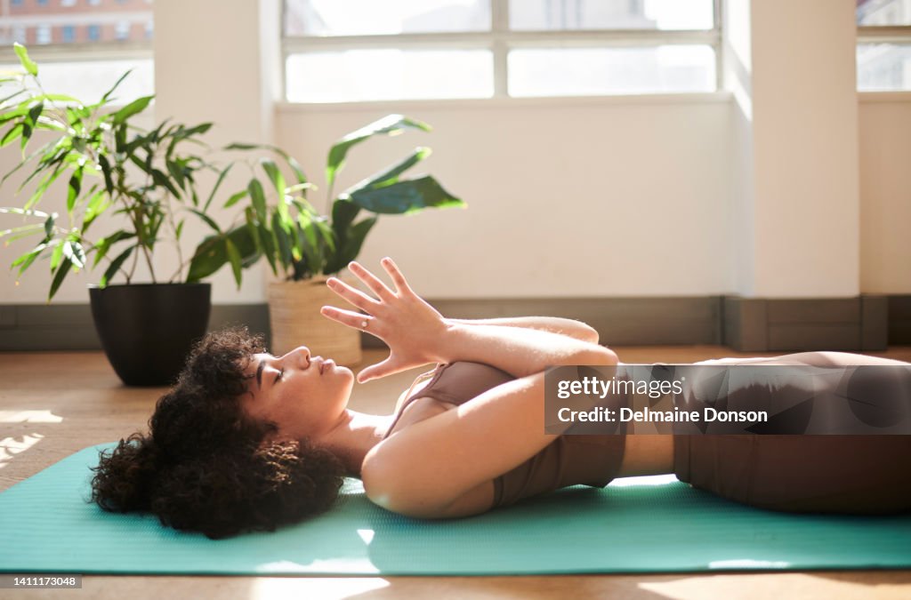 An active and mindful woman meditating in her house as part of her morning exercise routine. A fit female doing yoga at home training her balance and body strength. An athletic lady doing a workout