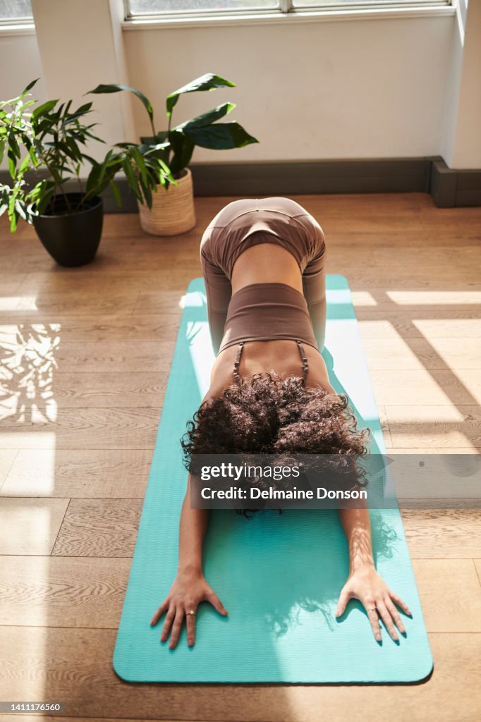 Woman practicing yoga in a studio or at home from above. Fit female bending and stretching forward while kneeling in balasana or extended childs pose. Exercising for inner peace and healthy lifestyle