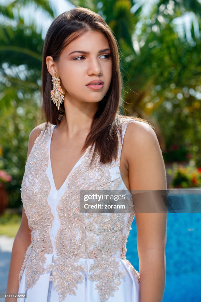 Schöne junge Brünette im weißen Spitzenkleid, die am Pool steht und wegschaut