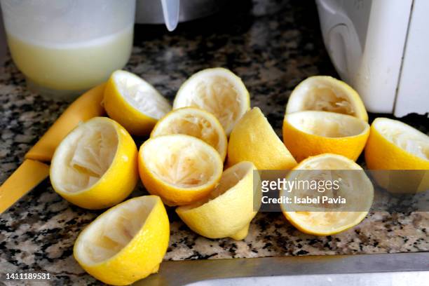 jug of lemonade and squeezed lemons on table in kitchen - saftpresse stock-fotos und bilder