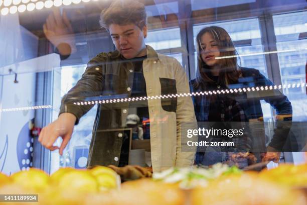 teenager mit freund, der gebäck von der ausstellungstheke auswählt - bakery display stock-fotos und bilder