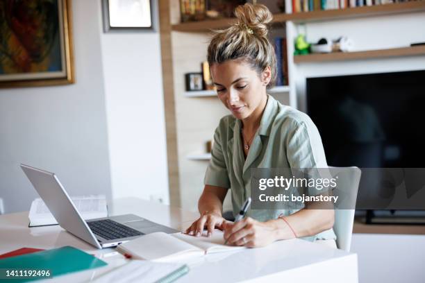 schöne junge frau, die sich notizen macht, während sie von zu hause aus lernt - understand stock-fotos und bilder