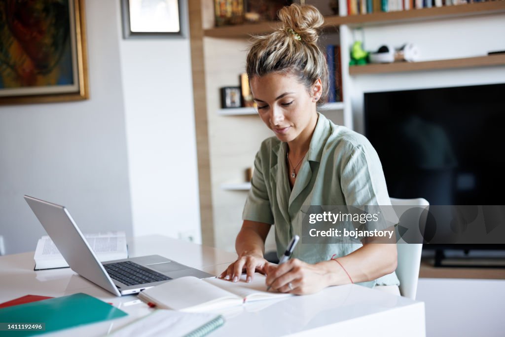 Beautiful young woman taking notes while learning from home