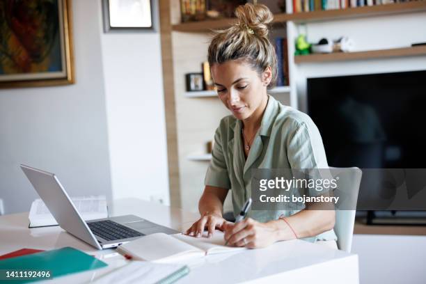 beautiful young woman taking notes while learning from home - 研究 個照片及圖片檔