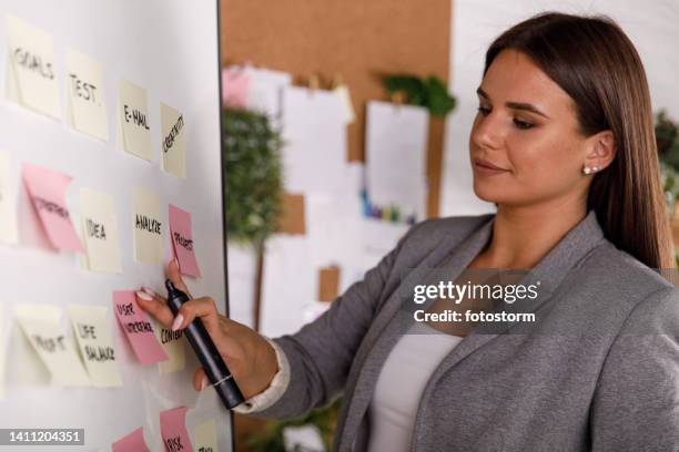 junge geschäftsfrau beim brainstorming von ideen, indem sie sie auf haftnotizen schreibt und sie auf ein whiteboard legt - young women only stock-fotos und bilder