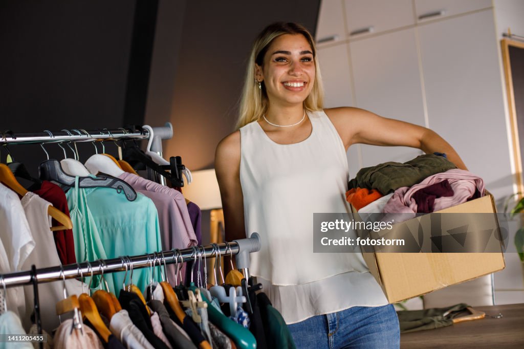 She Has A Rack Young Woman Standing By A Clothes Rack Holding A Box Full Of Clothes ...