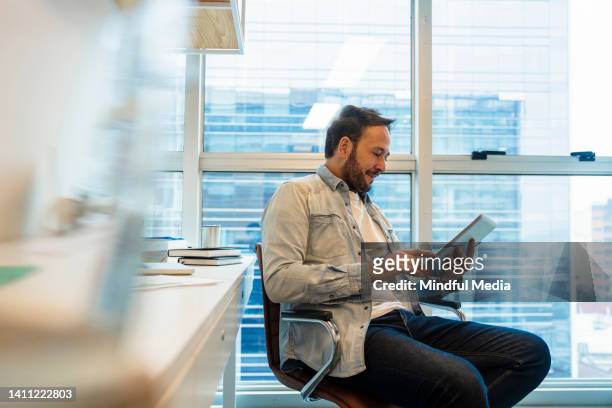 vista lateral de la toma media del hombre operando en su tableta digital dentro de una oficina - etf fotografías e imágenes de stock