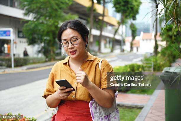 asian woman waiting for a taxi along the street in singapore with her phone - sudeste asiático etnia oriental - fotografias e filmes do acervo