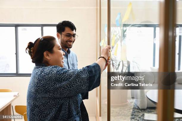 colleagues brainstorming using adhesive notes on an office window - フィリピン人 ストックフォトと画像