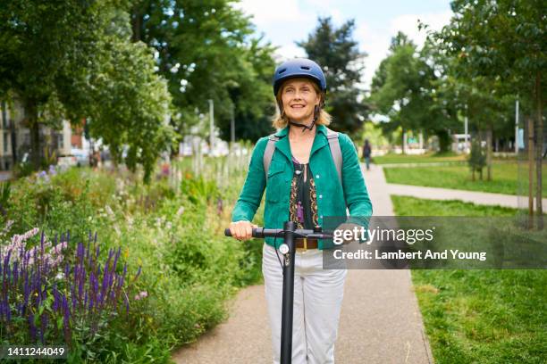 woman smiling riding an e scooter through the city paths - adult riding bike through park stock pictures, royalty-free photos & images