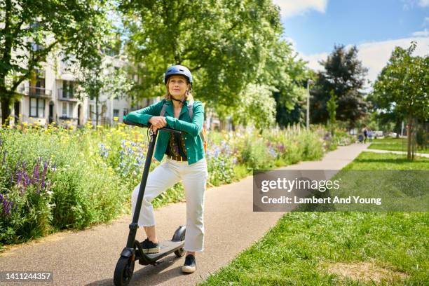 mature woman posing with her e scooter in a city park - e scooter stock-fotos und bilder