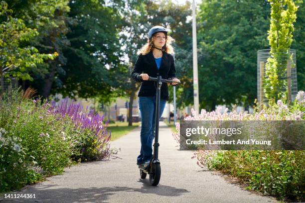 young woman smiling riding an e scooter through the city paths - mobility scooters stockfoto's en -beelden