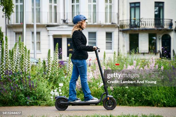 side view of a teenage girl using an e scooter through the city - tretroller stock-fotos und bilder