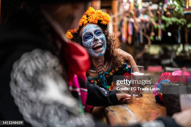 young woman talking and celebrating the day of the dead with her friends at bar - day of the dead stock pictures, royalty-free photos & images