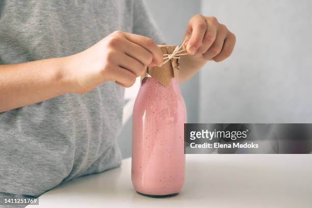 close-up of a girl's hands closing a smoothie bottle and tying it with a hemp rope. snack on the road, breakfast for school - hemp milk stock pictures, royalty-free photos & images
