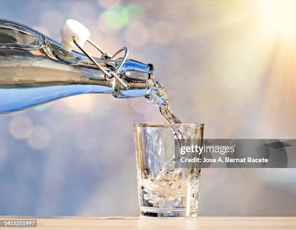 bottle fills a glass of drinking water illuminated by sunlight. - filling jar stock pictures, royalty-free photos & images