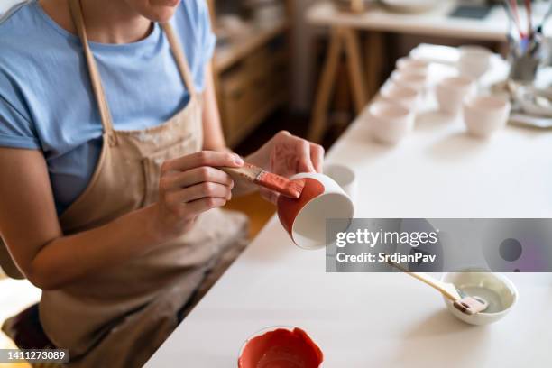 unrecognizable female craftperson, painting pottery products with red paint - earthenware stock pictures, royalty-free photos & images