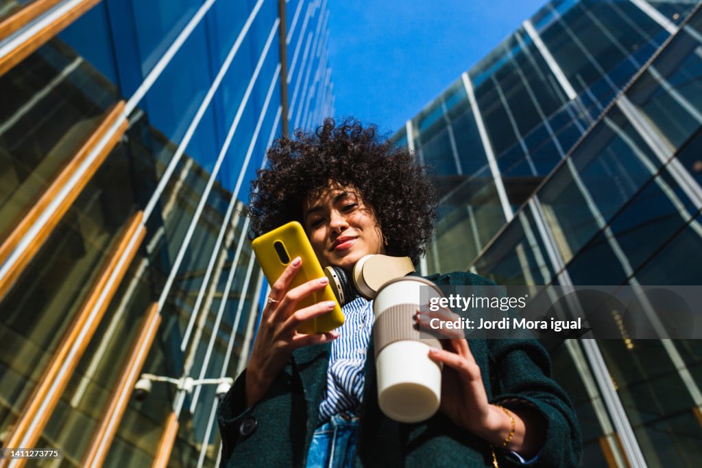 Low angle view of woman standing between commercial buildings using mobile phone.