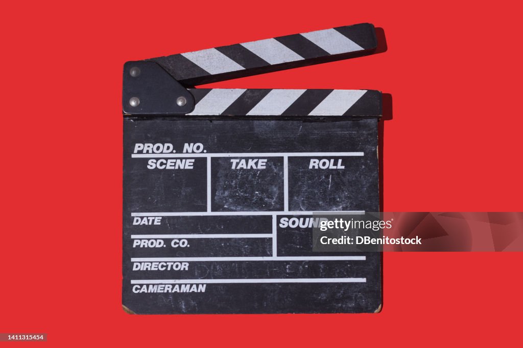 Old wooden movie clapperboard with hard shadow on red background. Concept of film industry, cinema, entertainment, and Hollywood.