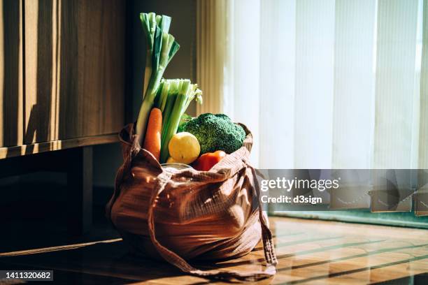 eco-friendly reusable shopping bag with multi-coloured fresh organic fruits and vegetables at home. shopping with reusable grocery bag for plastic free and waste-free life. responsible shopping. zero waste food shopping and sustainable lifestyle concept - bolsa reutilizable fotografías e imágenes de stock