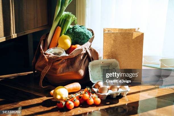 eco-friendly reusable shopping bag with multi-coloured fresh vegetables and groceries at home. shopping with reusable grocery bag for plastic free and waste-free life. responsible shopping. zero waste food shopping and sustainable lifestyle concept - shopping paper bag stock-fotos und bilder