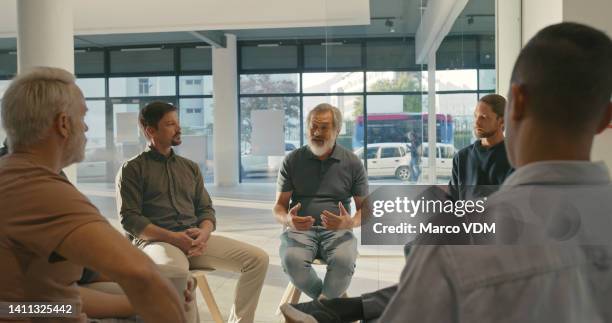 mature man talking and sharing his struggles with addiction at a aa meeting while sitting on chairs during group therapy. diverse male patients getting help and counseling at a rehab facility - addict stock pictures, royalty-free photos & images