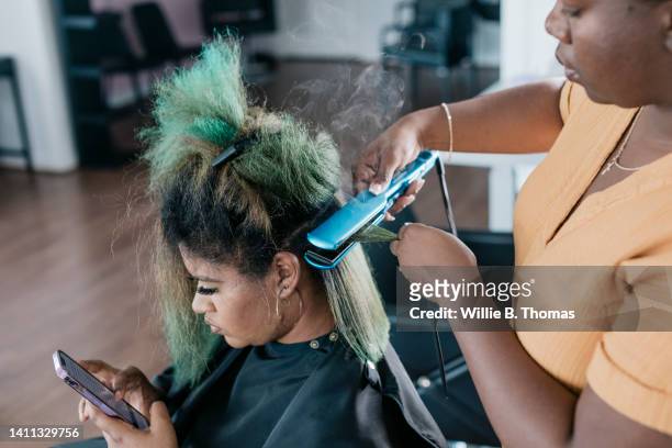 black woman getting curly hair straightened at salon - dyed red hair fotografías e imágenes de stock