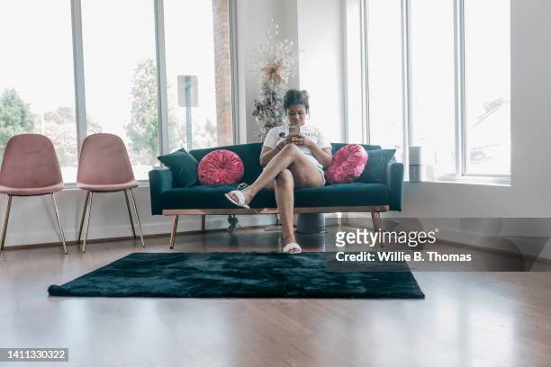 black woman waiting for hair appointment on sofa in salon - fashion woman floor cross legged stock pictures, royalty-free photos & images