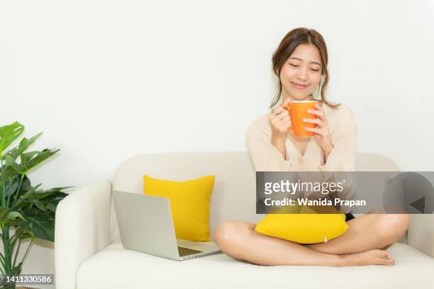 happy young woman drinking hot orange cup coffee after working and meeting online at home.  lifestyle freelance relax and chill  in living room.  lifestyle concept - leisure work coffee happy stockfoto's en -beelden