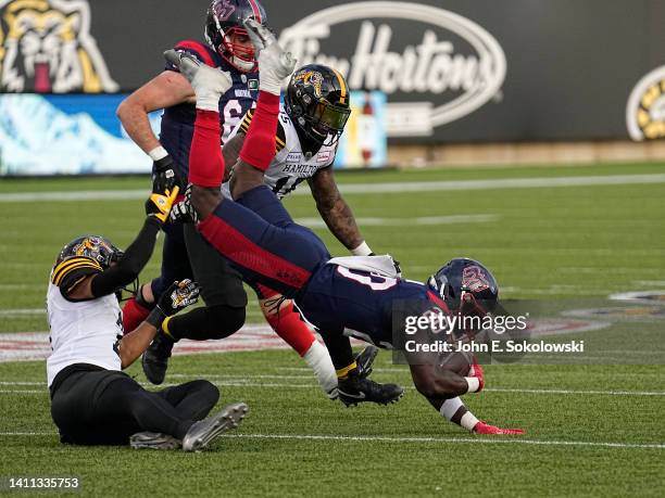 Jeshrun Antwi of the Montreal Alouettes gets upended by Ciante Evans and Kyle Wilson of the Hamilton Tiger-Cats at Tim Hortons Field on May 28, 2022...