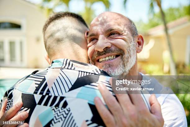 smiling gay man embracing partner in sunny miami back yard - 40s couple sunny stockfoto's en -beelden