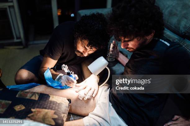 man tattooing leg - tattoo needle stock pictures, royalty-free photos & images