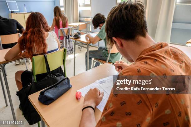 rear view of a male high school student writing a test in the classroom. - aluna imagens e fotografias de stock