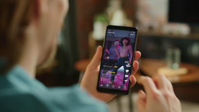 Person Using Social Media App on Smartphone, Looking at Live Stream Videos. Realistic Feed Scrolling on Mock-up Application Posts: Creativity, Dancing, Meme, Lifestyle, Device Review, Viral Content
