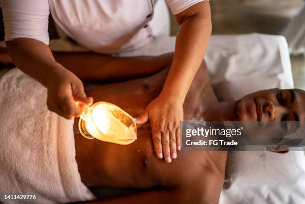 masajista vertiendo aceite en la espalda del cliente - black massage therapist fotografías e imágenes de stock