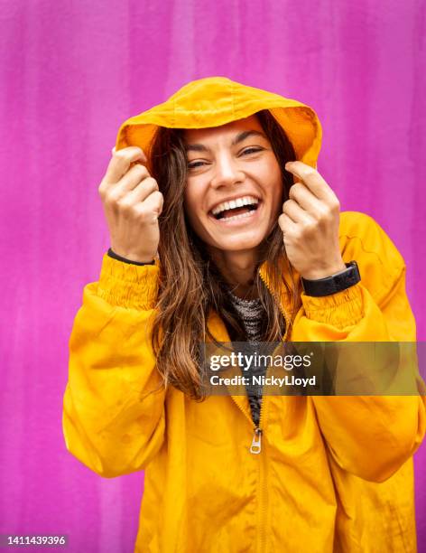 laughing young woman wearing a raincoat standing outside in the rain - regnkläder bildbanksfoton och bilder