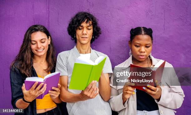 three young friends reading books while leaning against a purple wall - read book outside young woman stock pictures, royalty-free photos & images