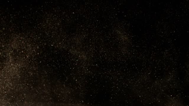 Super slow motion of glittering golden particles on black background.