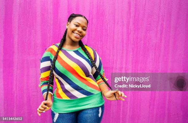 smiling young woman with long braids standing against a pink wall - braids stock pictures, royalty-free photos & images