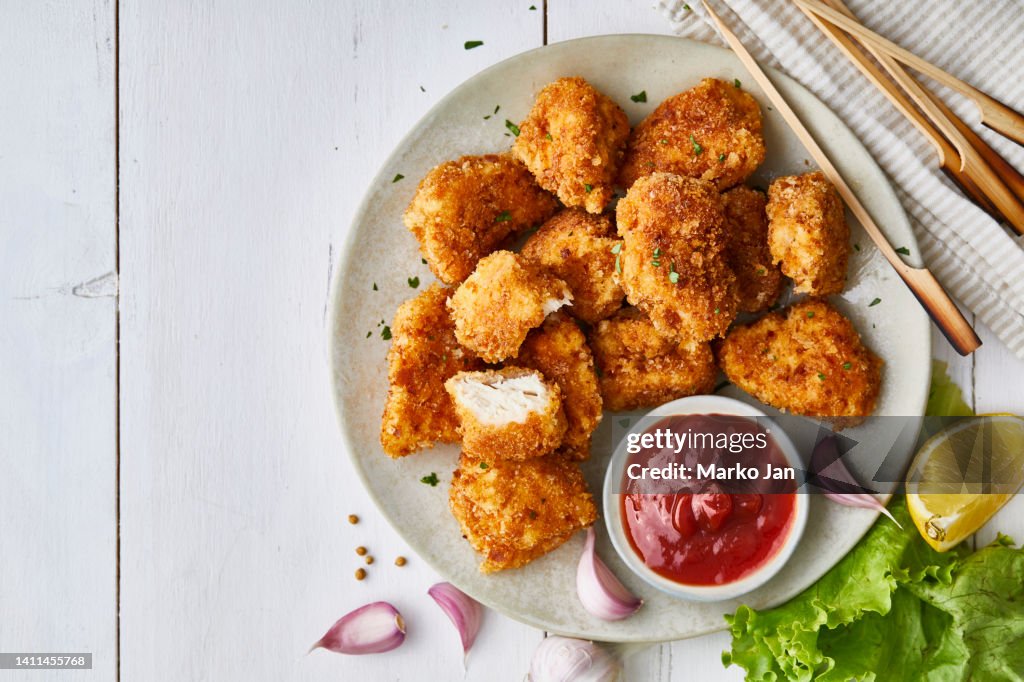 Chicken nuggets in a plate, with ketchup, salad and lemon, served on a white wooden table