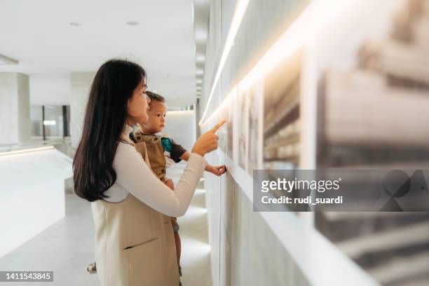 asian women watching the exhibition with her baby in art gallery - baby pointing stockfoto's en -beelden