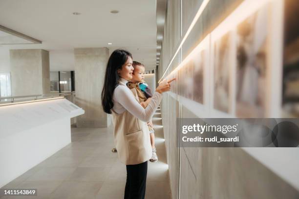 asian women watching the exhibition with her baby in art gallery - baby pointing stockfoto's en -beelden