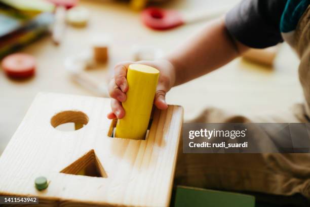 un bebé está jugando con un bloque de juguete de madera - vida de bebé fotografías e imágenes de stock