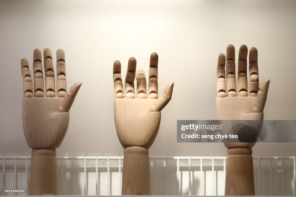 Close-Up Of Wooden figurine Hand Against Grey Background