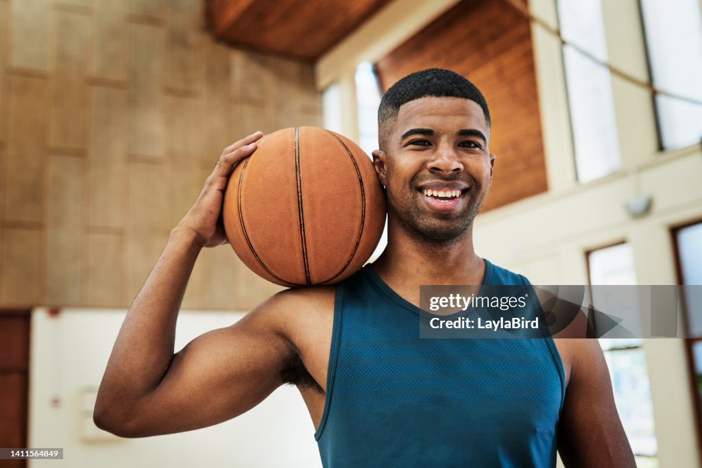 A Happy African American basketball player holding a ball in a sports club. Portrait of a fit and active athlete enjoying his sports training at the college courts. Athletic man smiling at practice